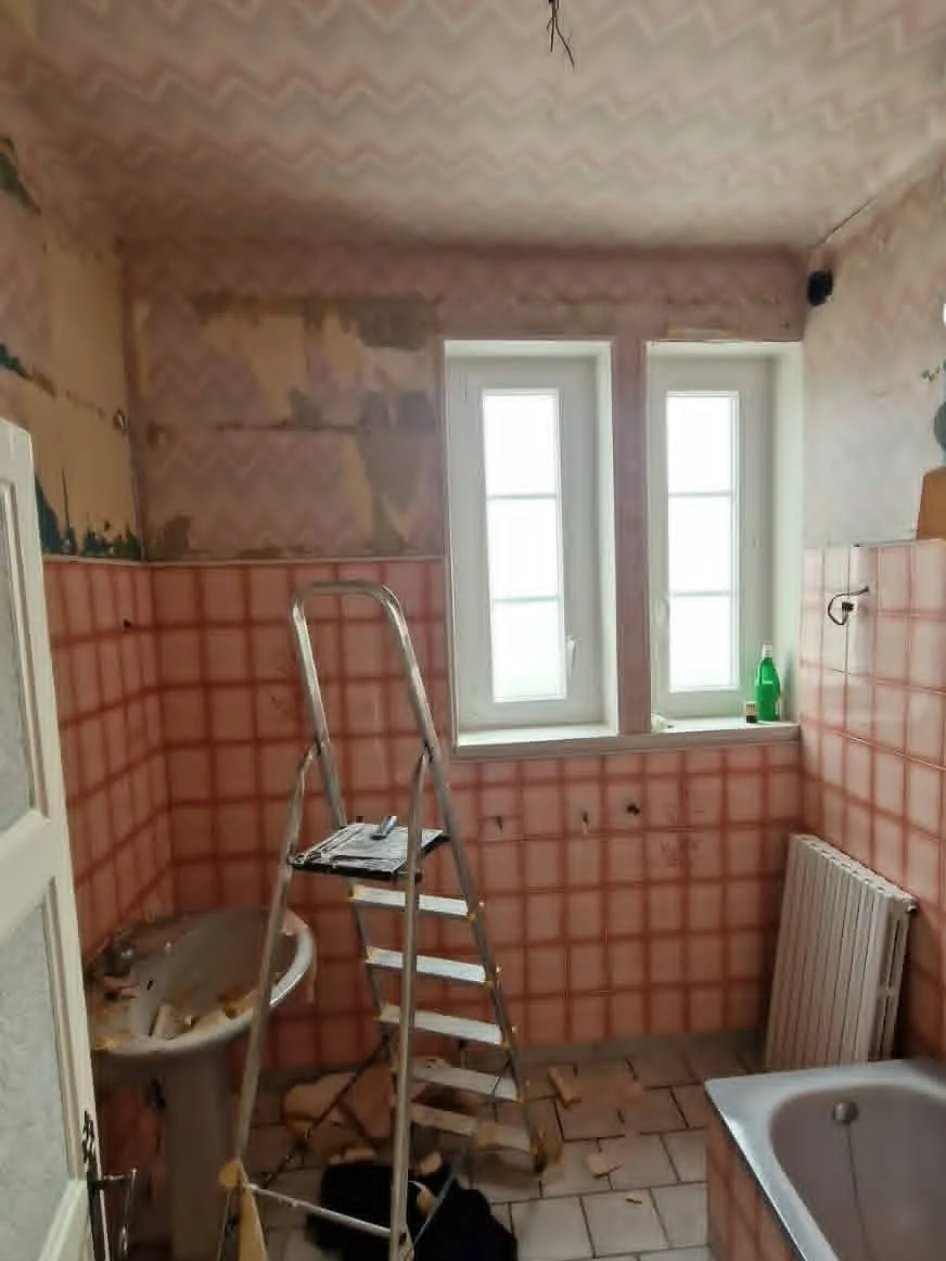 Salle de bain — côté fenêtre avant travaux : Carrelage mural rose d’origine, murs et plafond fatigués.