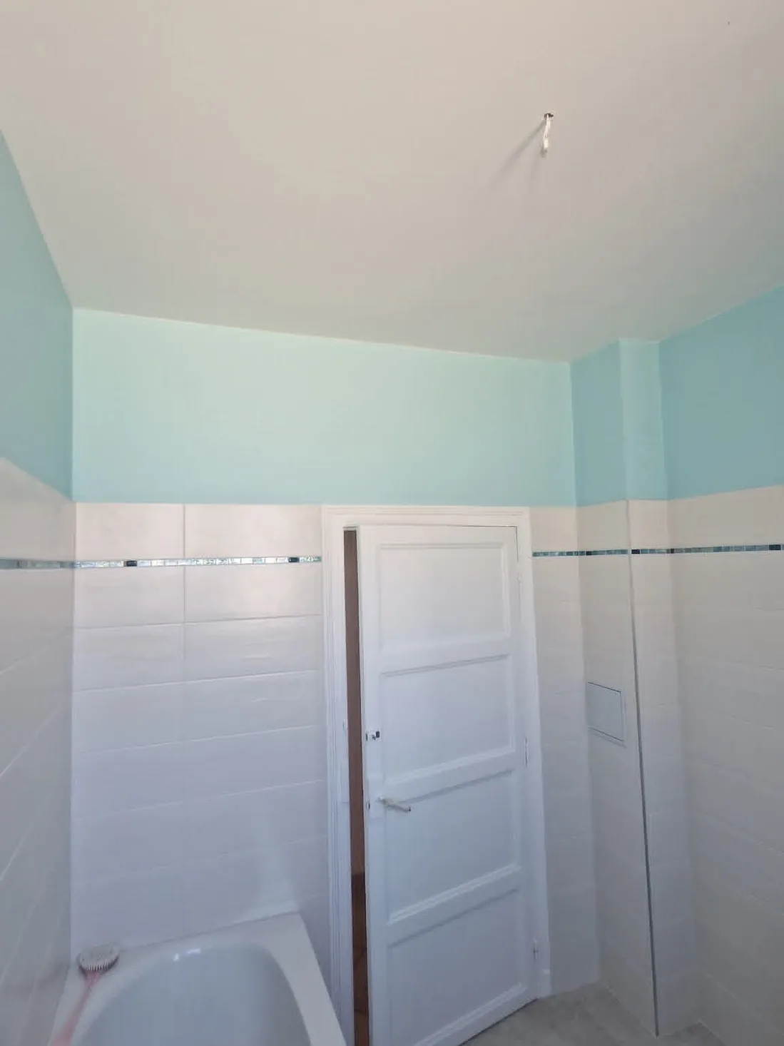 Salle de bain — côté porte après travaux : Murs assainis, porte laquée blanche et camaïeu de vert d’eau.